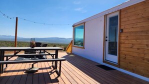 Une terrasse en bois avec une table et des chaises, une porte vitrée et une vue sur les montagnes.