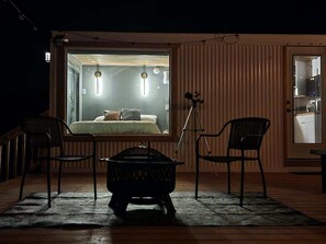 A cozy room with a bed, two chairs, a small table, and a tripod.