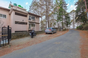 A two-story building with a balcony, a parked car, and a motorcycle on a dirt path.