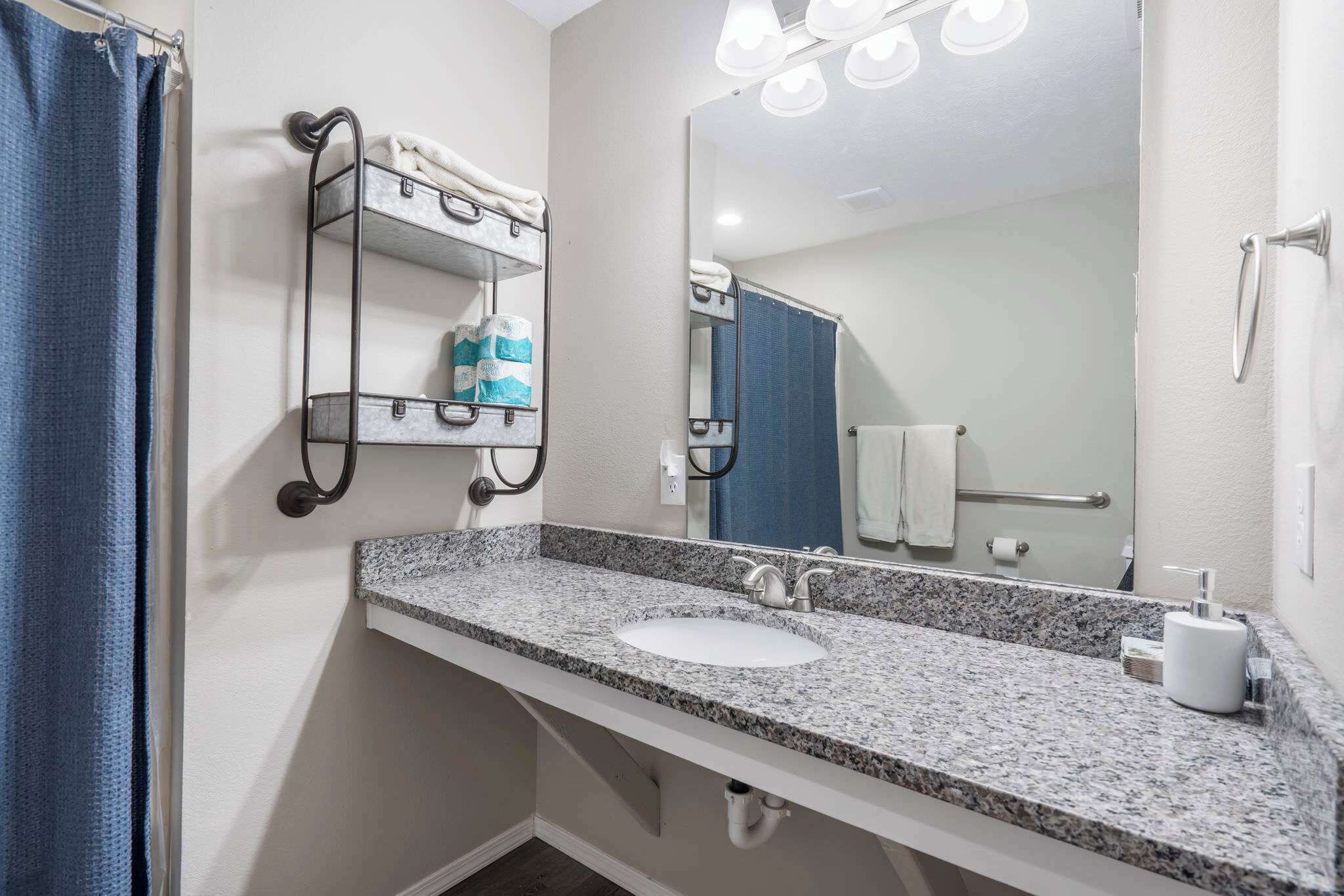 A bathroom with a granite countertop sink, a towel rack with towels, a mirror, and a shower curtain.