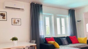 A living room with a sofa set, a dining table, and two windows with curtains. - T1 Sunset View (Albufeira)