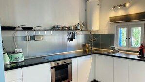 A modern kitchen with white cabinets, a black countertop, a built-in oven, and a window with a view of greenery. - T1 Sunset View (Albufeira)