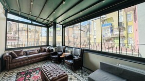 A spacious living room with a leather sofa, a grey couch, and a patterned rug. Large windows offer views of the cityscape. - The House Company (Istanbul)