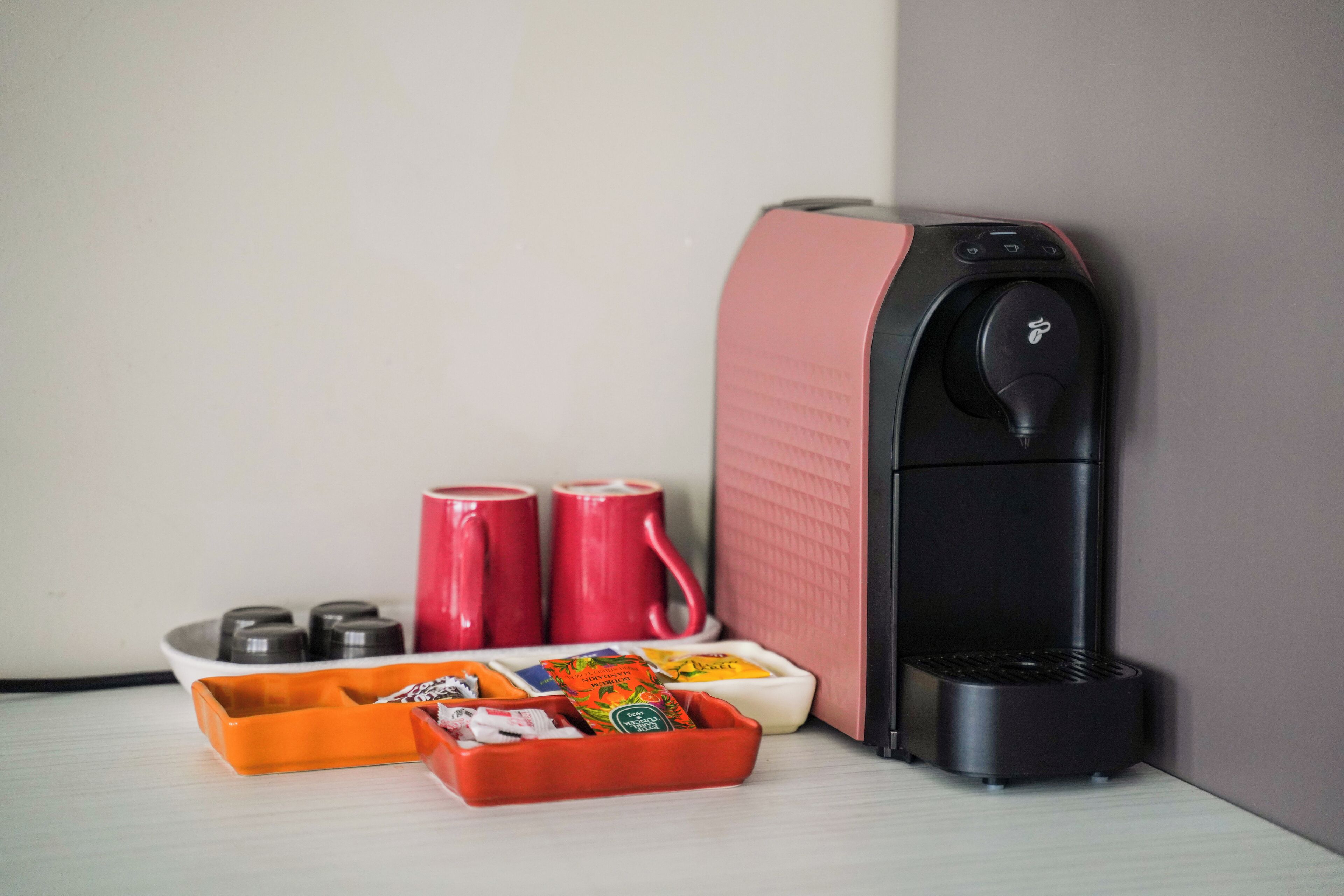 A coffee machine, two red mugs, and a tray with tea bags and snacks.