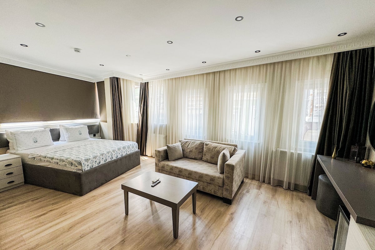 A modern hotel room with a bed, a sofa, a small table, and a desk.