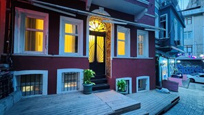 A building with a wooden deck, a set of stairs leading to a door with a decorative glass panel, and a small garden area with potted plants. - The House Company (Istanbul)