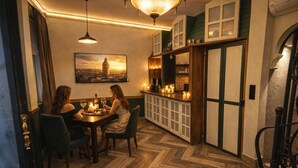 A dining area with a herringbone floor, a table with chairs, a painting of a cityscape, and a bar area with a cabinet. - The House Company (Istanbul)