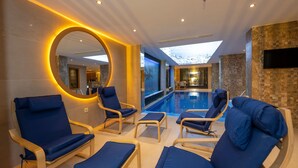 Un área de piscina interior moderna con sillas reclinables azules y un espejo grande.