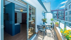 Un balcón con puerta corrediza de vidrio que da a una habitación, una mesita con sillas y plantas en macetas.