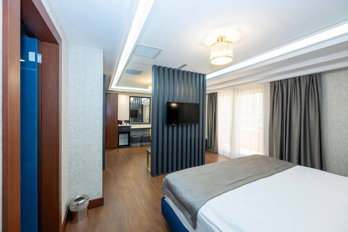 A modern hotel room with a large bed, a flat-screen TV, a desk with a chair, and a bathroom with a toilet and sink.