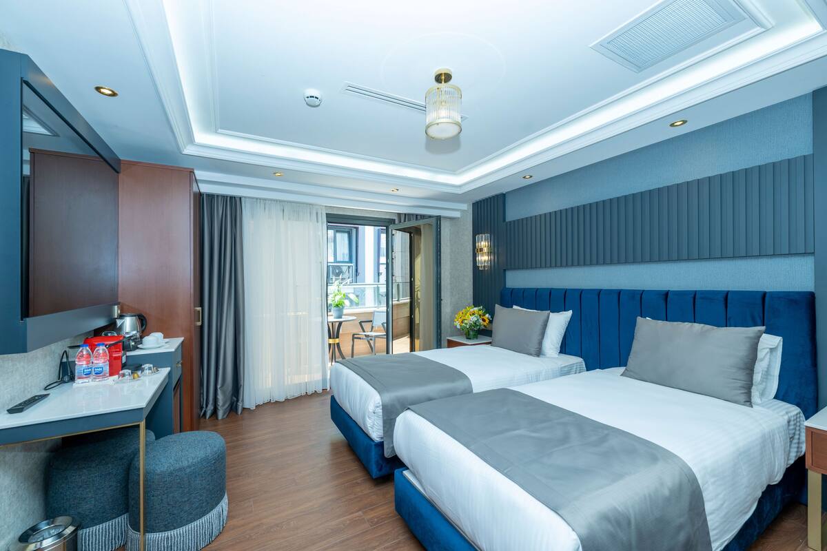 A modern hotel room with two beds, a desk, and a balcony with a view.