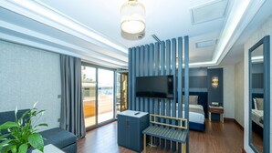Una habitación de hotel moderna con televisión de pantalla plana, un sofá, una mesita, un banco, un escritorio y una mesita de noche.
