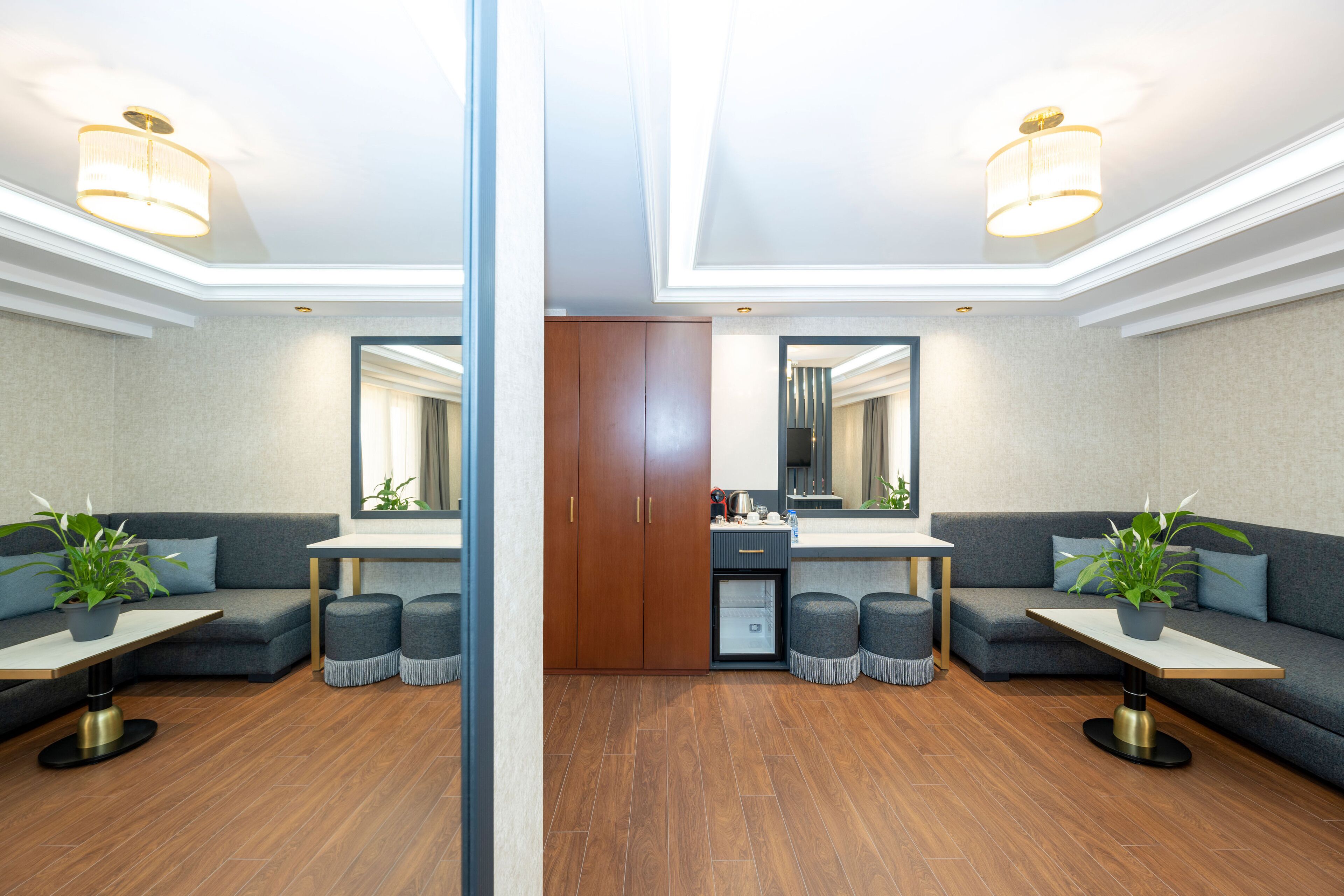 A modern hotel room with a mirrored wall, a sofa, a dining table, and a kitchenette.