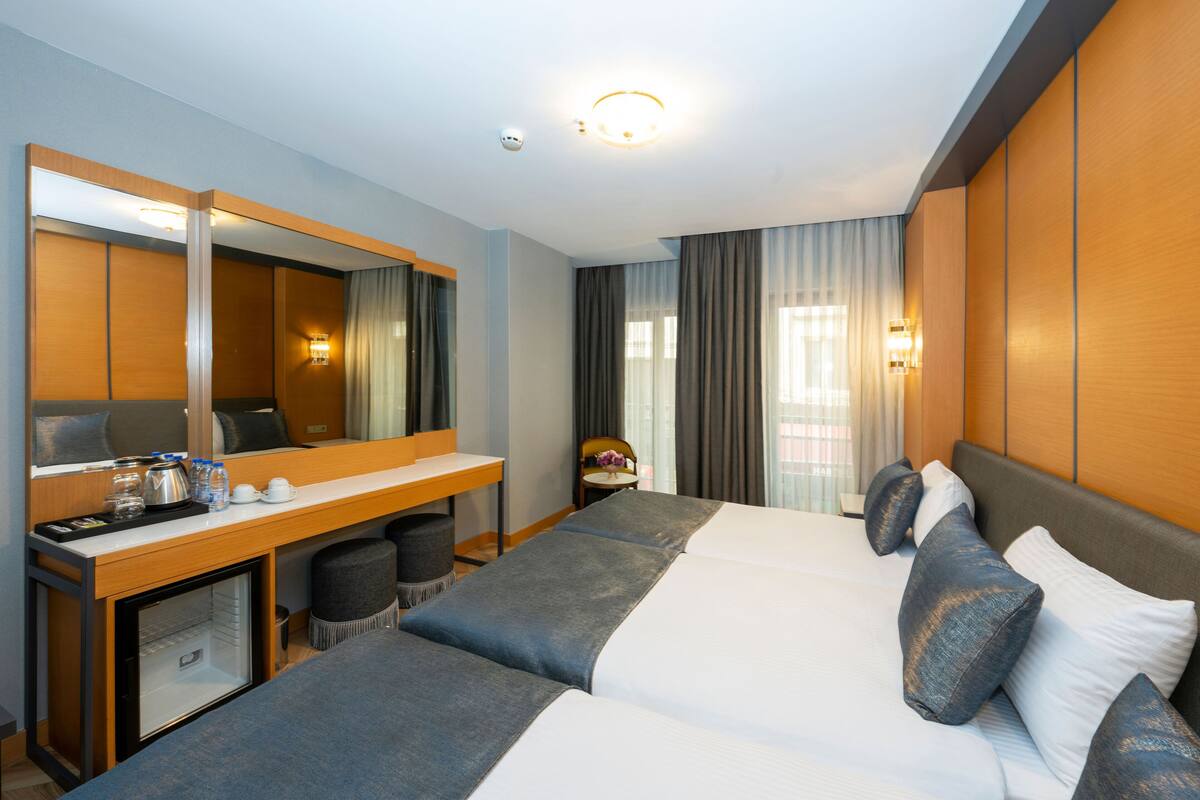 A hotel room with a large bed, a desk with a mirror, a small fridge, and a chair.
