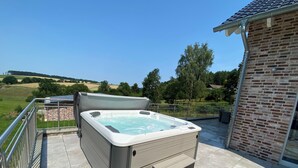 Ein Whirlpool auf einer Terrasse mit Blick auf ein Backsteingebäude und ein grünes Feld.