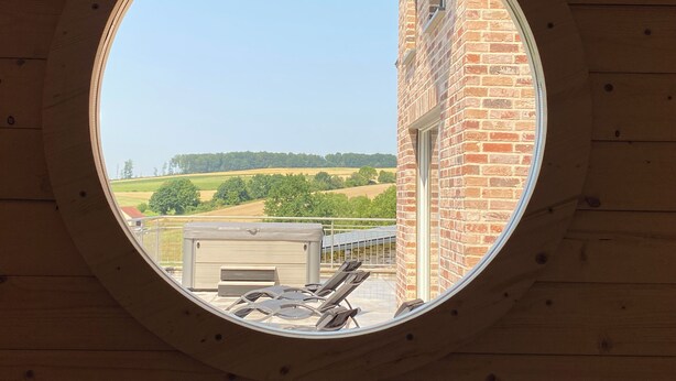 Ein rundes Fenster mit Blick auf ein Ziegelgebäude, eine grüne Wiese und einen klaren Himmel.
