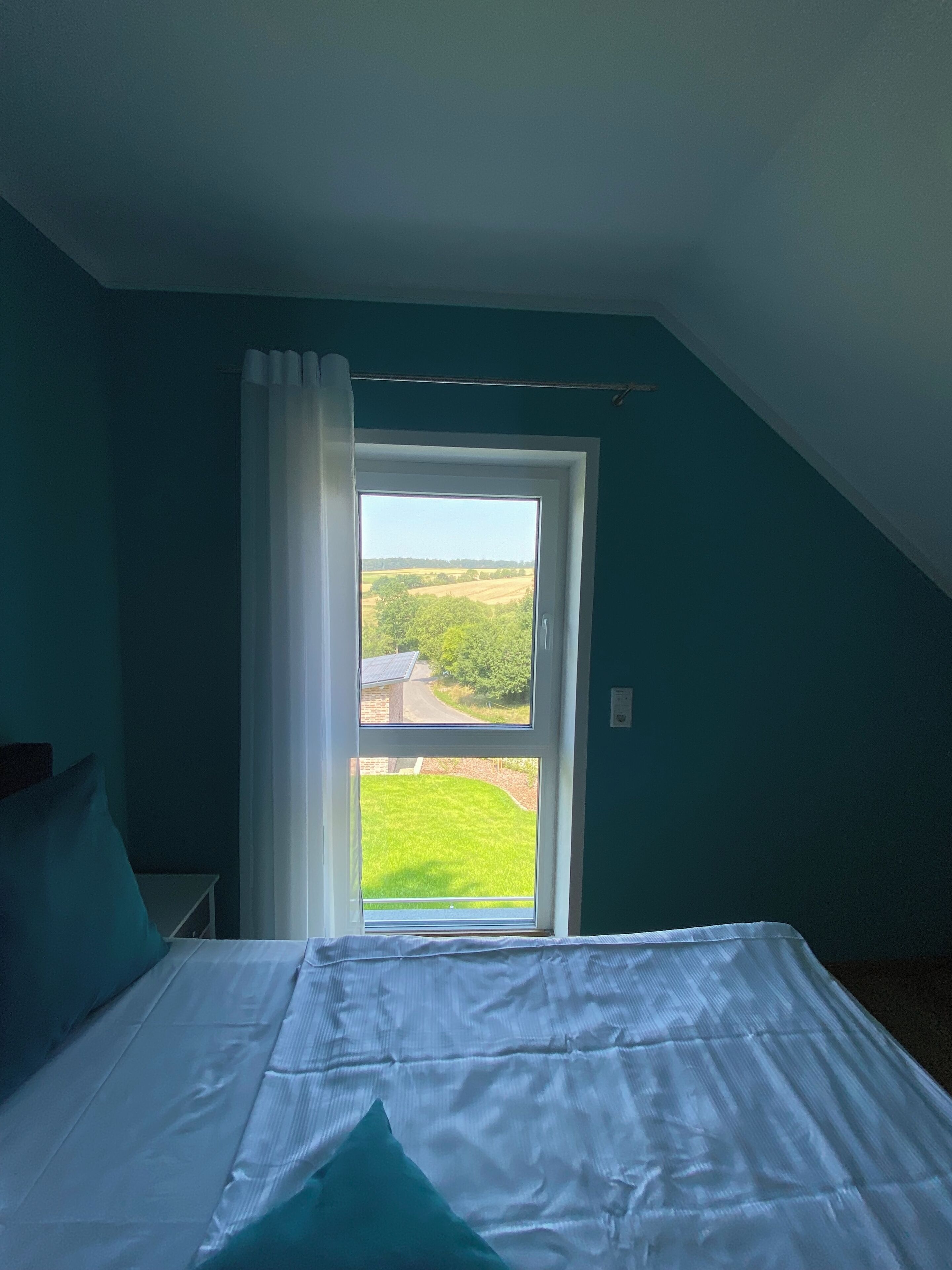 A bedroom with a large window, a bed, and a view of a green landscape.