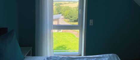 A bedroom with a large window, a bed, and a view of a green landscape.