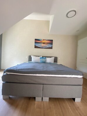 A bedroom with a bed, pillows, and a painting of a sunset over the ocean.