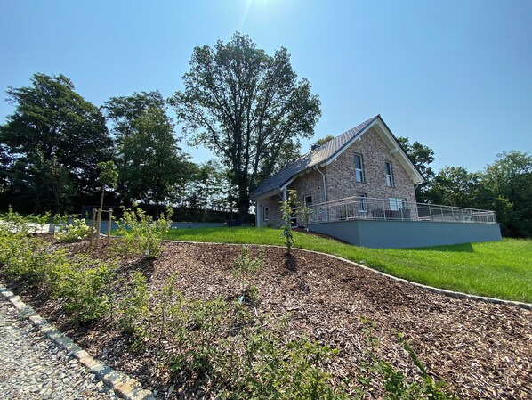 A house with a brick exterior, a balcony, and a well-maintained garden with mulch and plants.