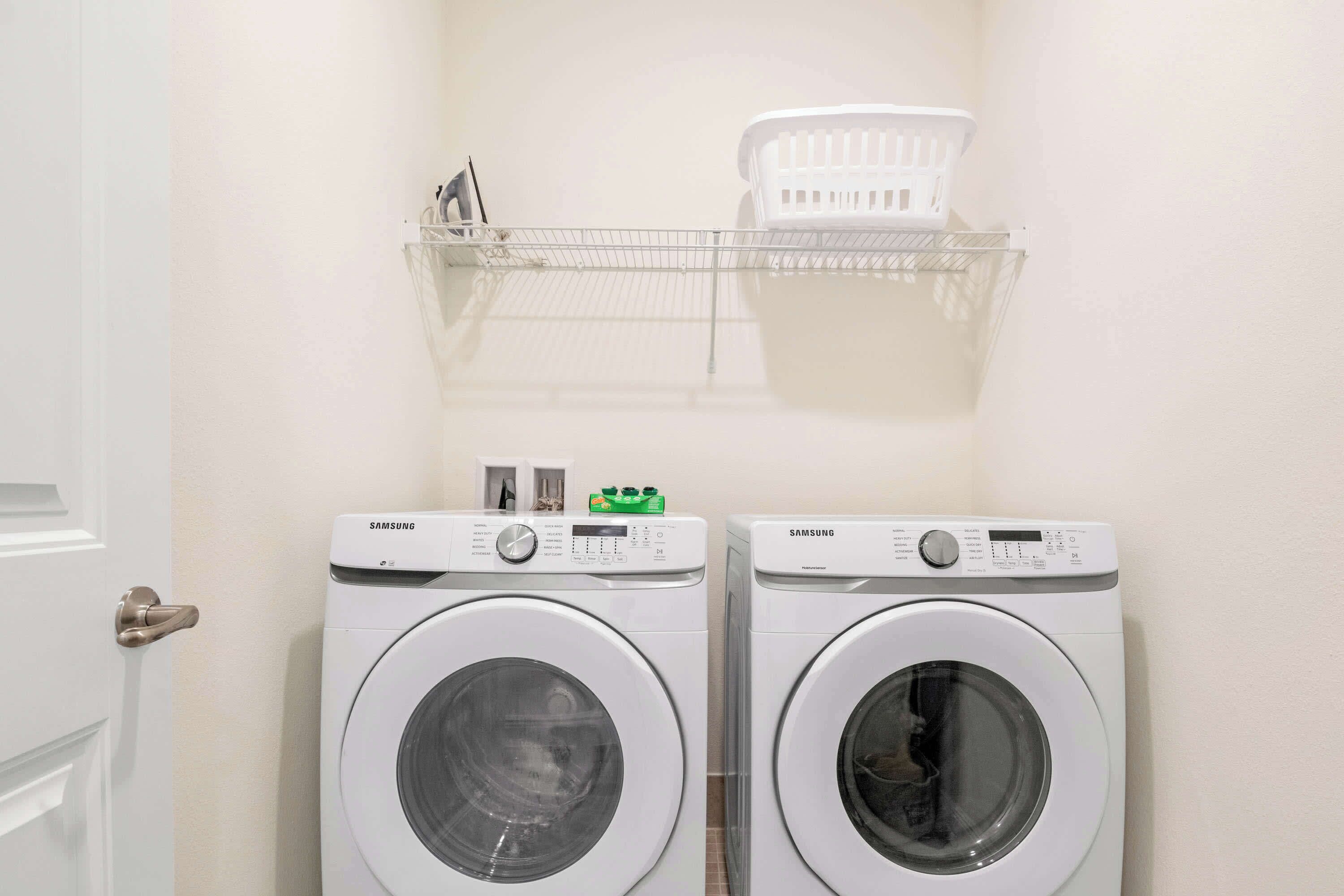 Deux machines à laver Samsung dans une buanderie, avec une porte blanche et un panier à linge sur une étagère.