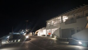 A nighttime view of a coastal building with a staircase leading to a balcony, illuminated by exterior lights. - Air house          . (Mykonos)