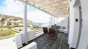 A covered outdoor area with a table and chairs, a sofa, and a view of the sea and buildings in the distance. - Air house          . (Mykonos)