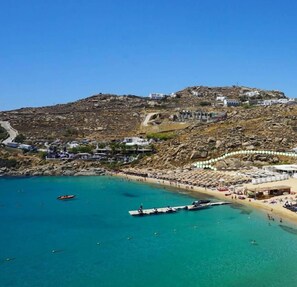 A coastal town with buildings on a hillside, a beach with umbrellas, and boats in the water. - 1Path houses Mykonos, Air Cycladic home near the Super Paradise beach sand (Mykonos)