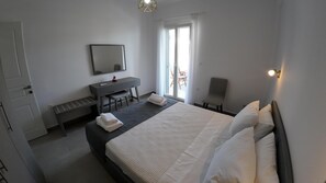 A modern hotel room with a large bed, a desk with a chair, a mirror, and a window with curtains.