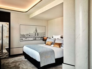 Una habitación de hotel moderna con una cama grande, una obra de arte urbana enmarcada, ducha de mármol y pared con textura.