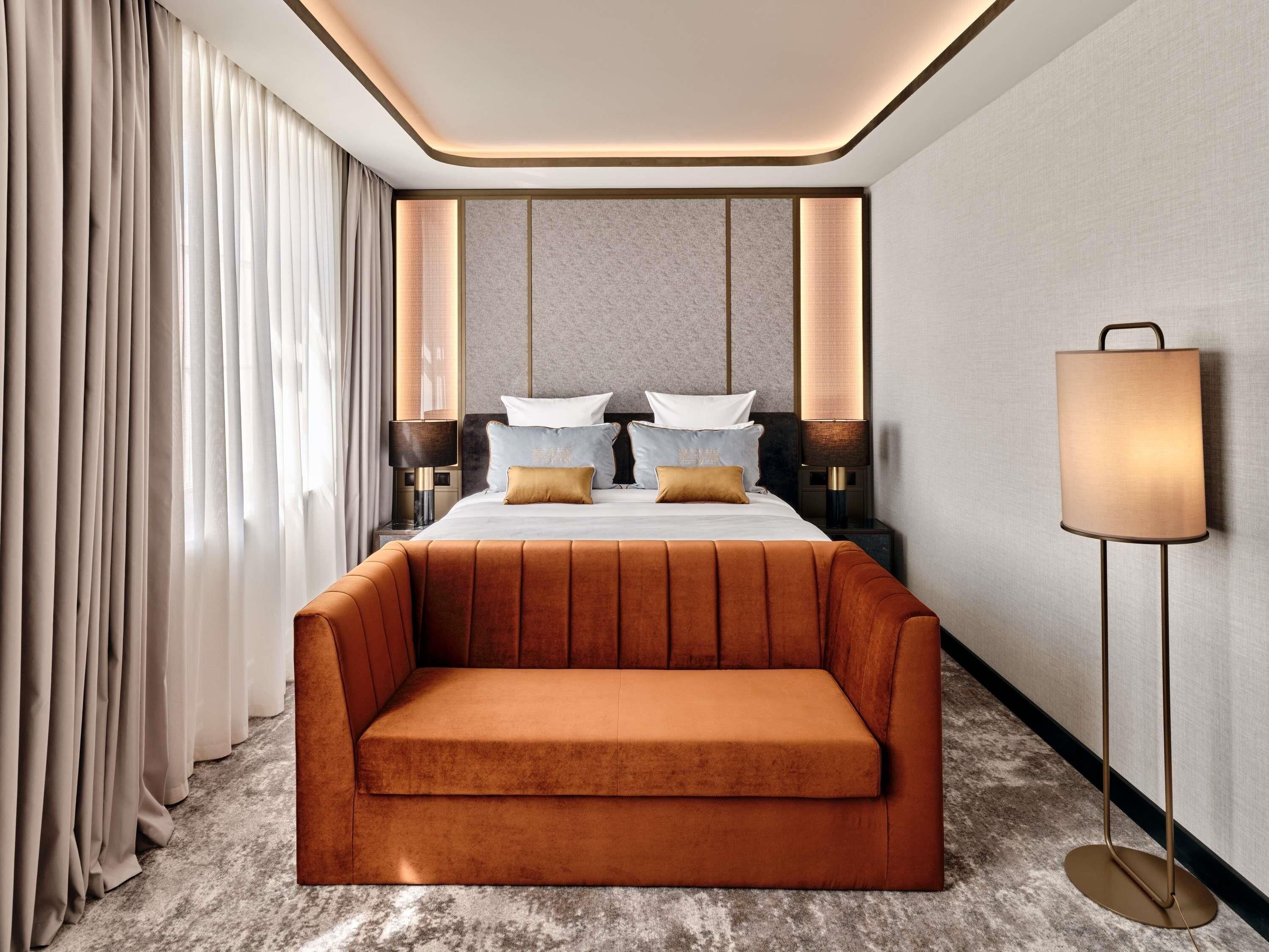 A modern hotel room with a large bed, a sofa, two bedside tables, and a floor lamp.