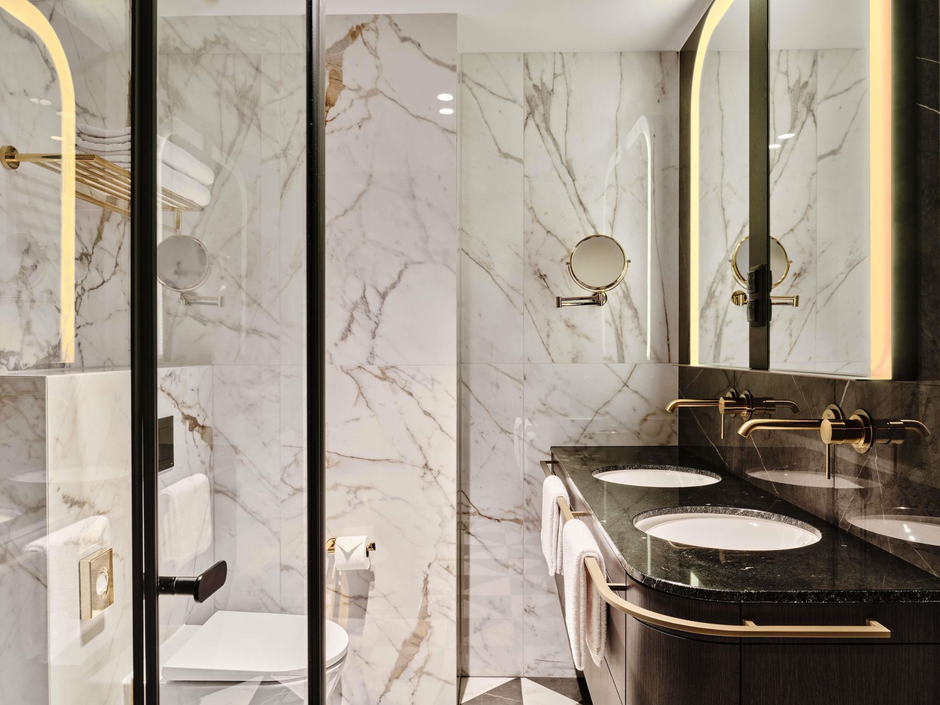 A modern bathroom with marble walls, a black countertop, and gold fixtures.