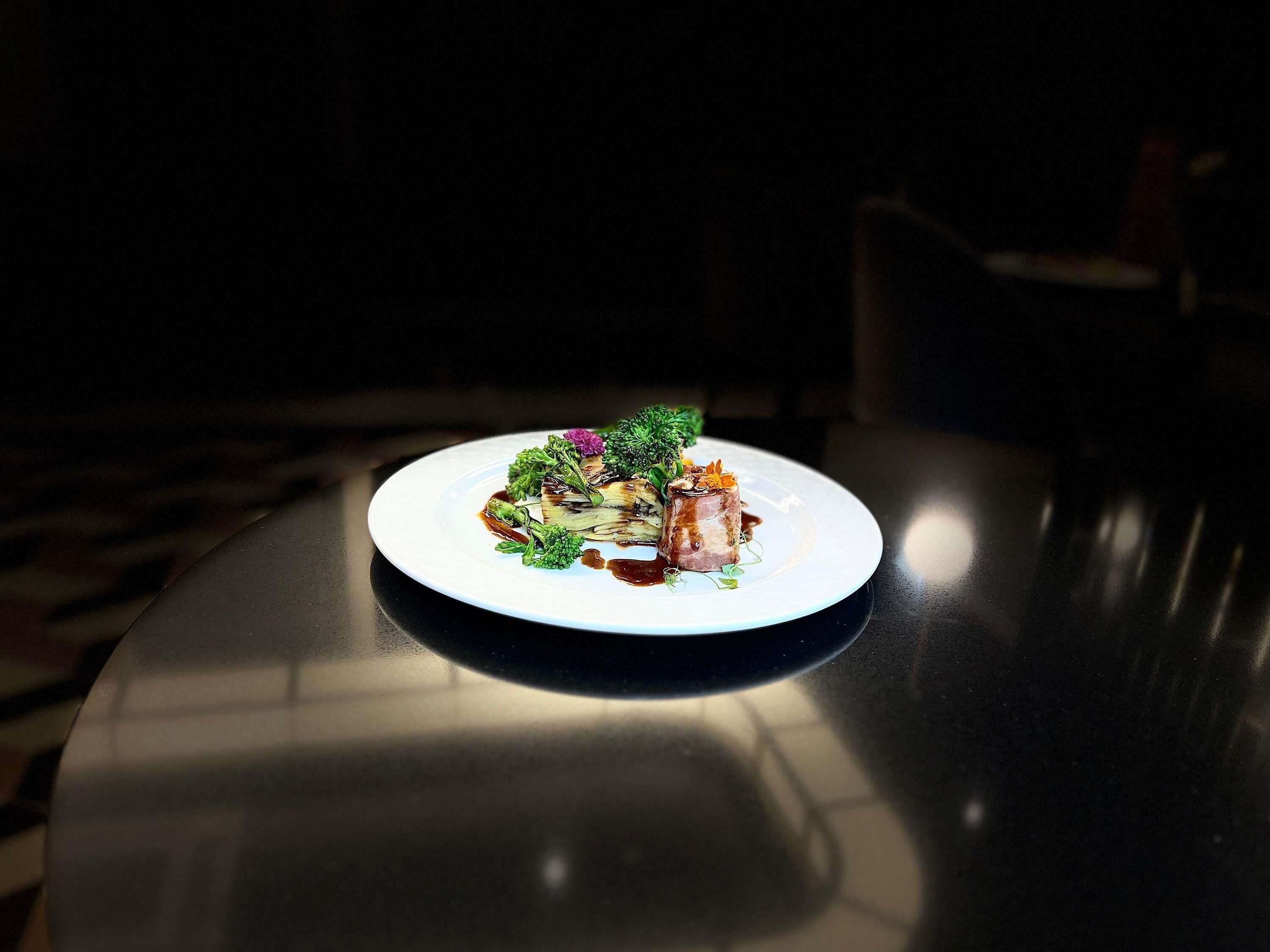 A white plate with a dish on a dark table in a dimly lit room.