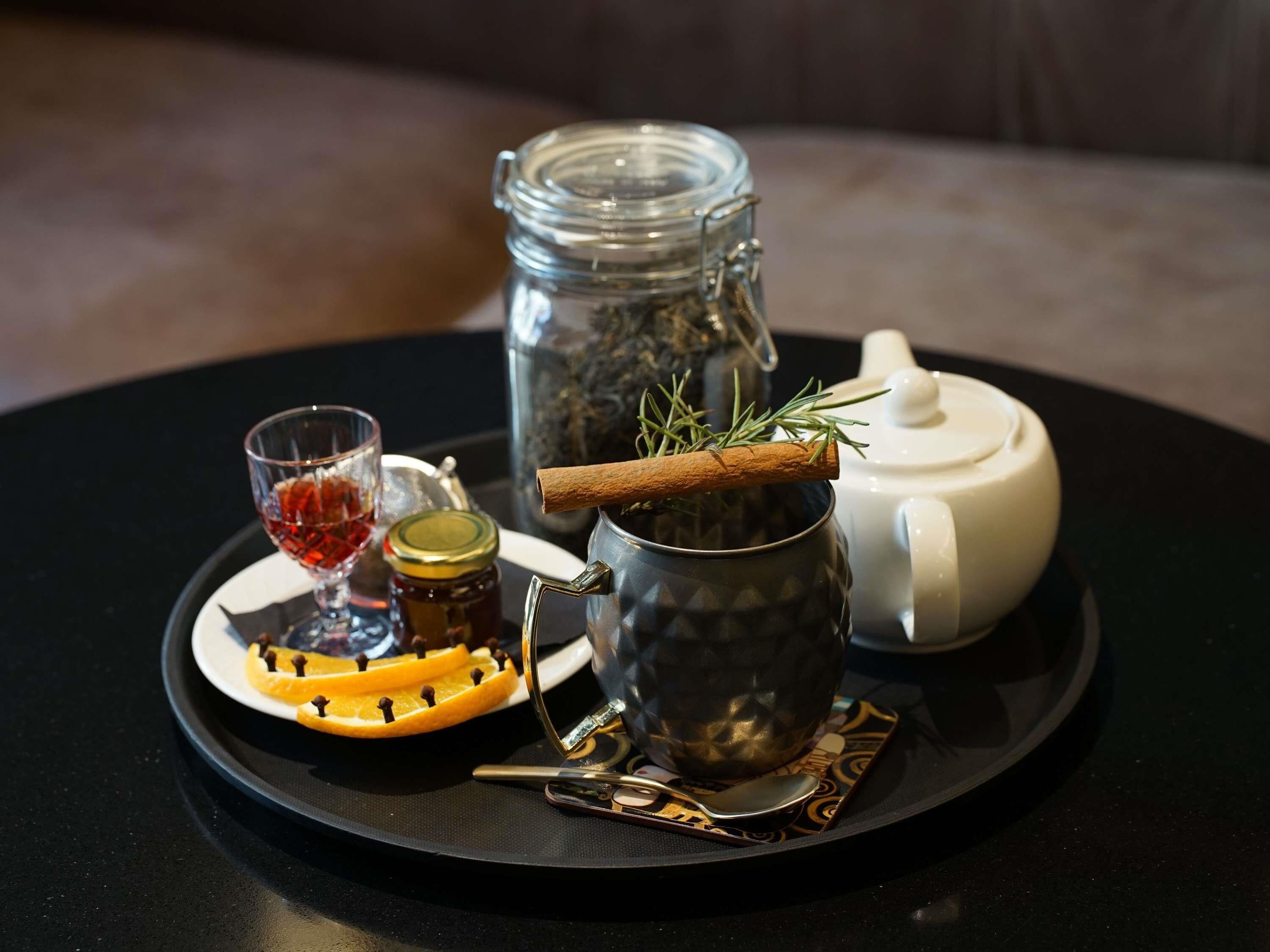 A tray with a teapot, a glass of red liquid, a jar of honey, and a cinnamon stick.