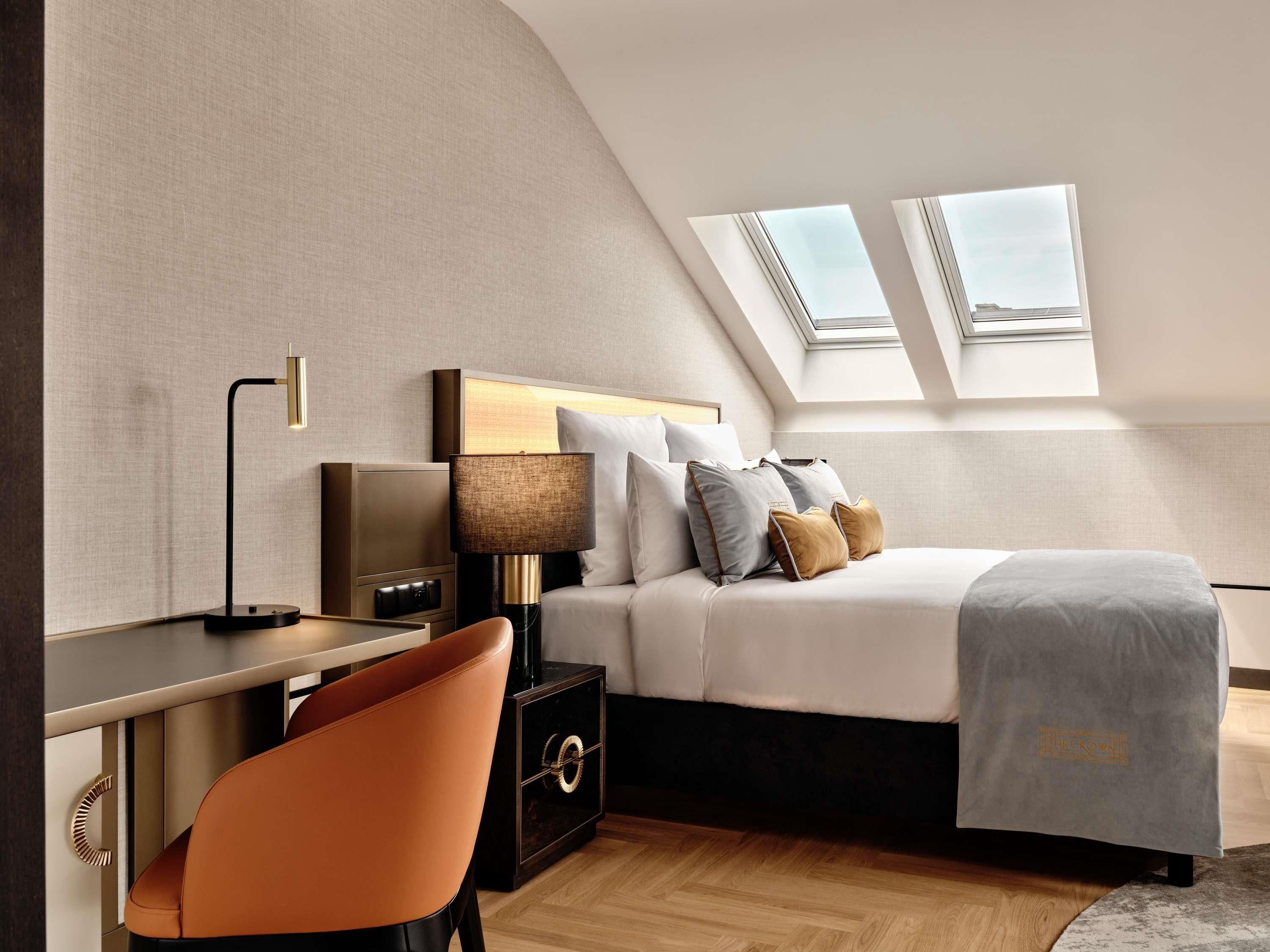 Une chambre à coucher moderne, avec un lit, un bureau, une chaise et une table de chevet. Des fenêtres de toit sont situées au-dessus du lit.