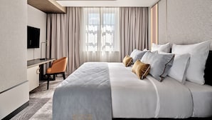 A modern hotel room with a large bed, a desk with a chair, and a television. - The Crown Krakow Center - Handwritten Collection ACCOR (Kraków)