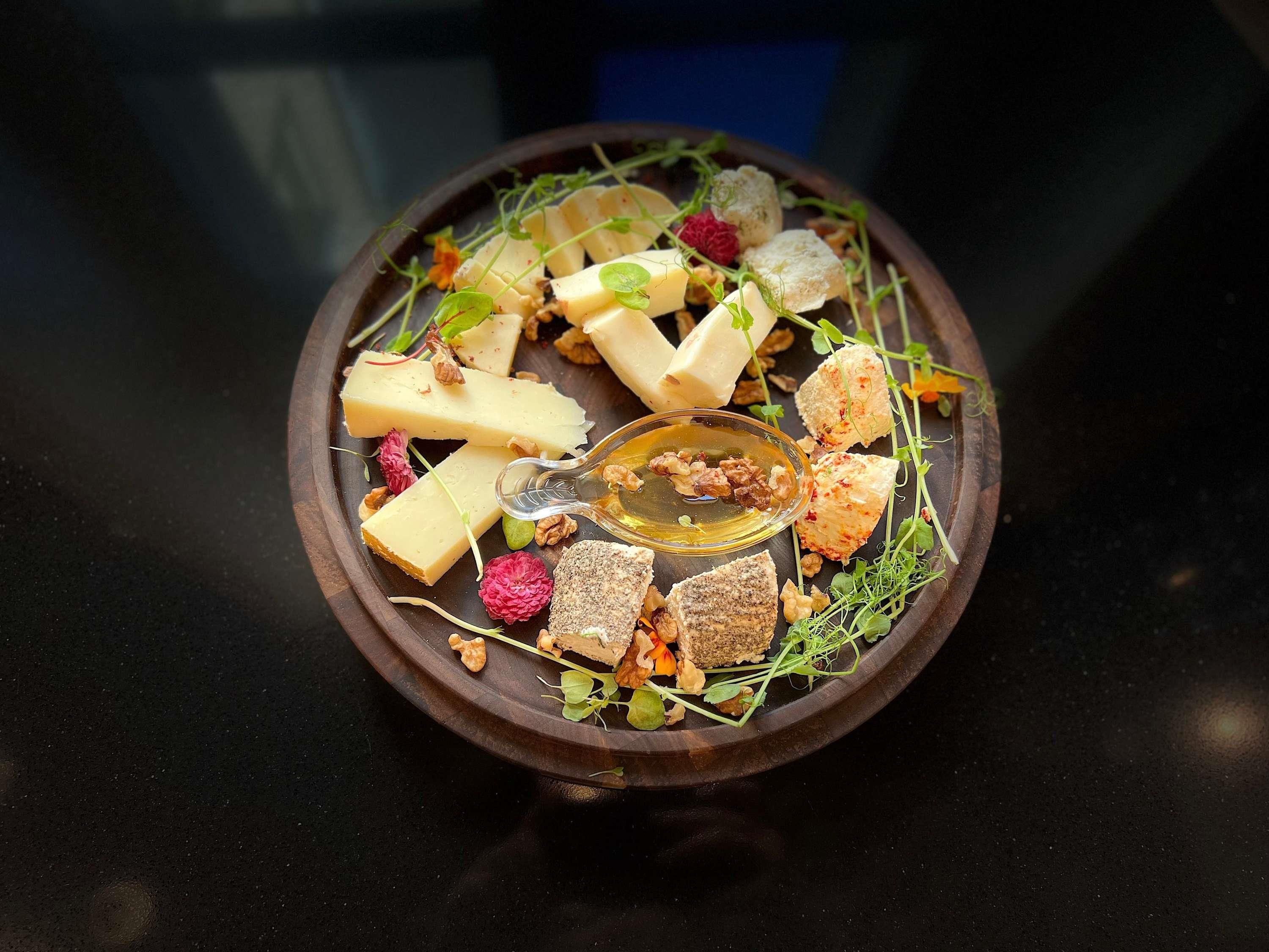 Une planche en bois sur laquelle sont disposés divers fromages, des noix et des fruits secs, le tout présenté sur une surface sombre.