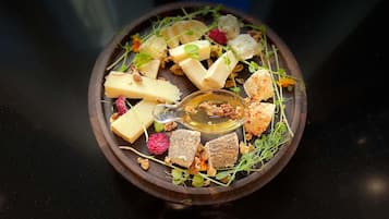 Una tabla de madera con varios quesos, nueces y frutas secas sobre una superficie oscura.
