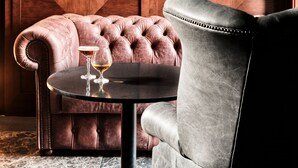 A room with a tufted leather armchair, a round table with a glass, and a wall with geometric patterns and two wall-mounted lights. - The Crown Krakow Center - Handwritten Collection ACCOR (Kraków)