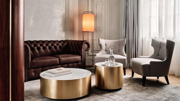 A modern living room with a brown leather sofa, a white coffee table, a gold side table, and a grey armchair. - The Crown Krakow Center - Handwritten Collection ACCOR (Kraków)