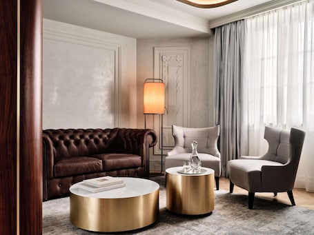 A modern living room with a brown leather sofa, a white coffee table, a gold side table, and a grey armchair.