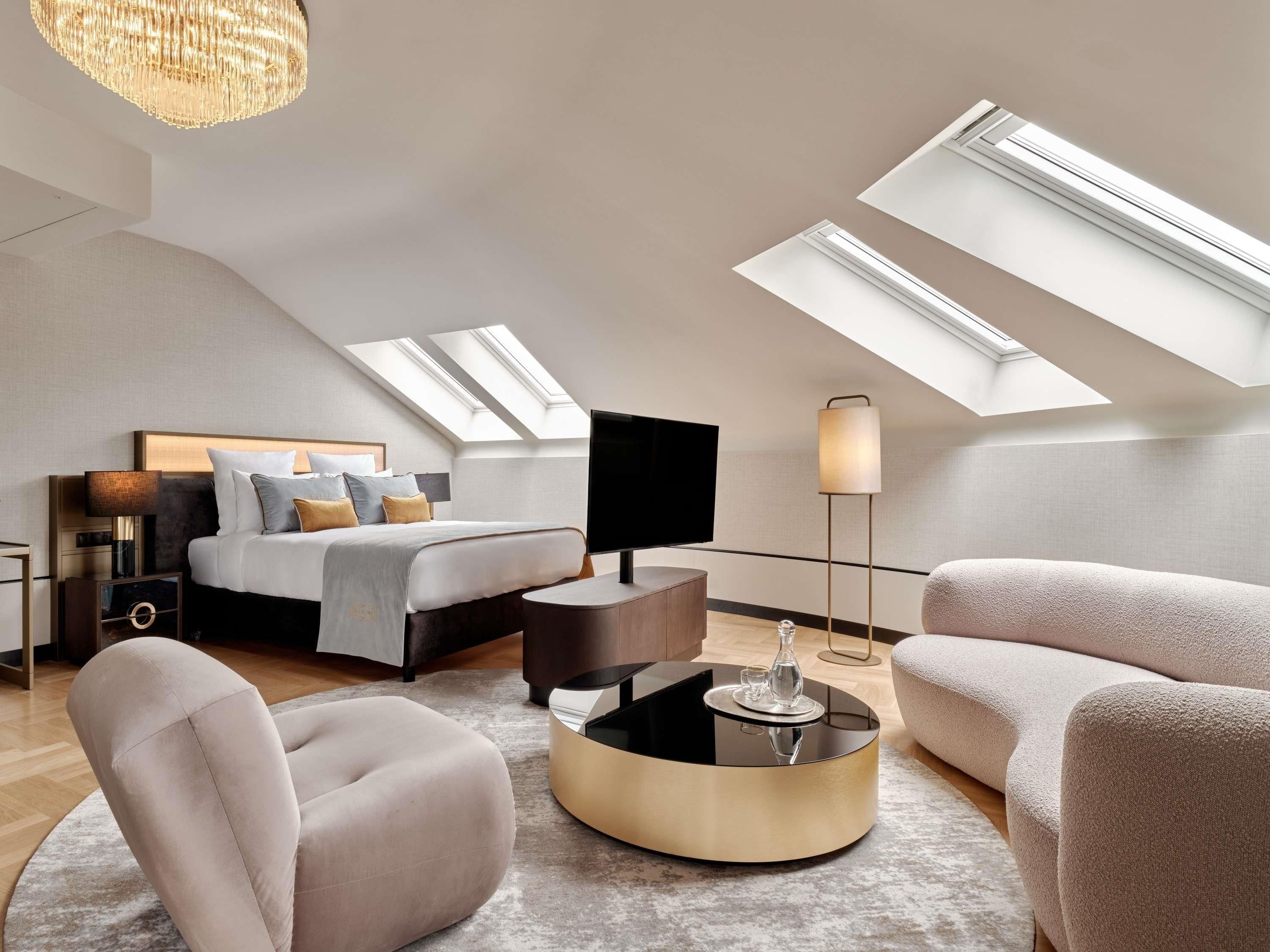 A modern bedroom with a bed, a TV, a lamp, a round coffee table, and a sofa.