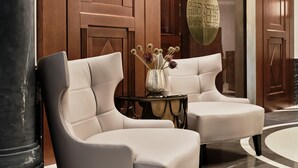 Two plush armchairs in a lobby with a wooden panel wall and a glass door with a brass handle. - The Crown Krakow Center - Handwritten Collection ACCOR (Kraków)
