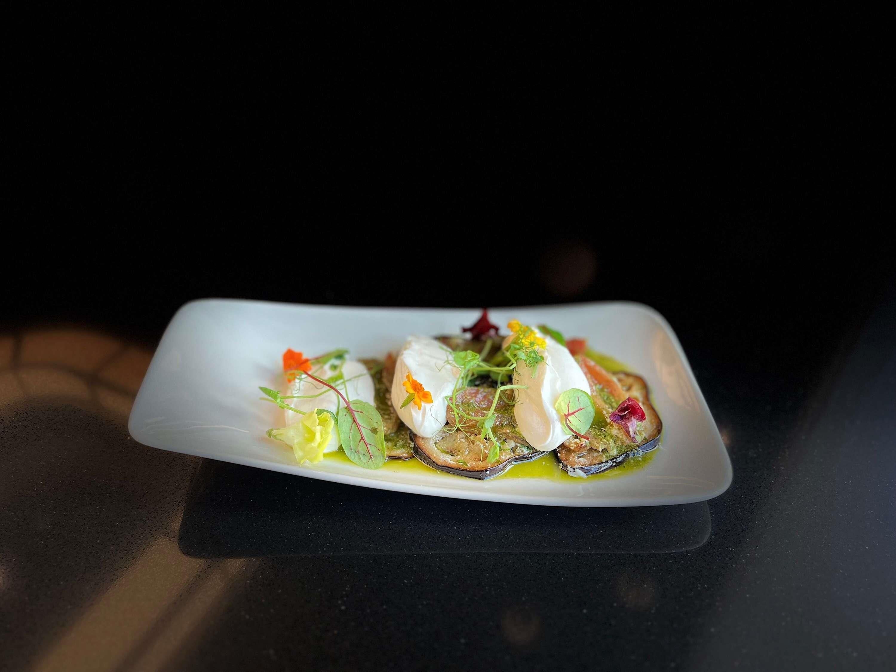 A white rectangular plate with a seafood dish, garnished with greens and flowers, on a dark surface.