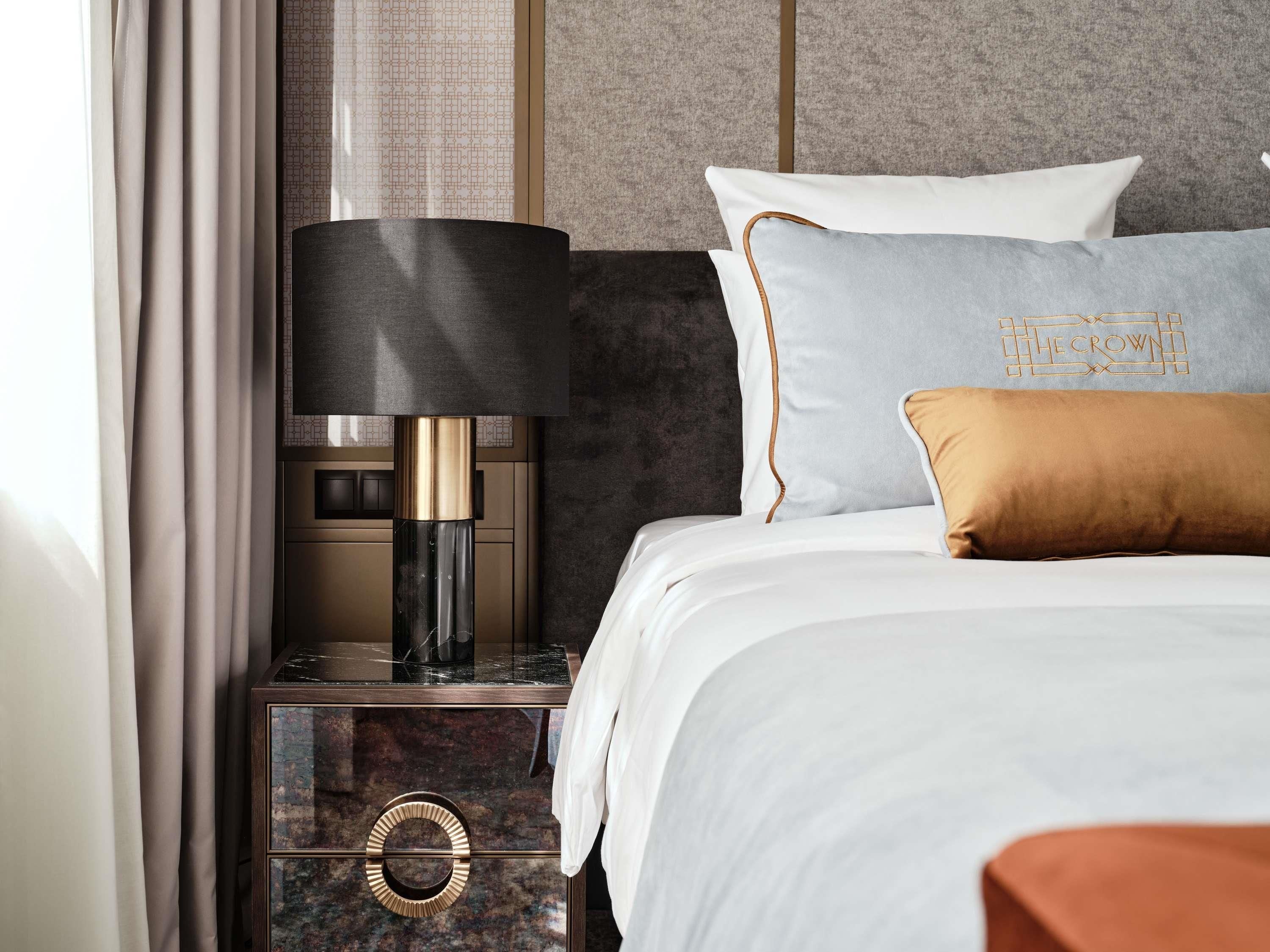 A modern hotel room with a bed, a nightstand with a lamp, and a decorative wall panel.