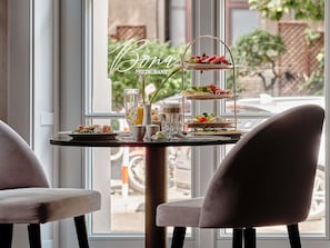 A restaurant setting with a tiered dessert display, a glass of water, and a plate of food. - The Crown Krakow Center - Handwritten Collection ACCOR (Kraków)