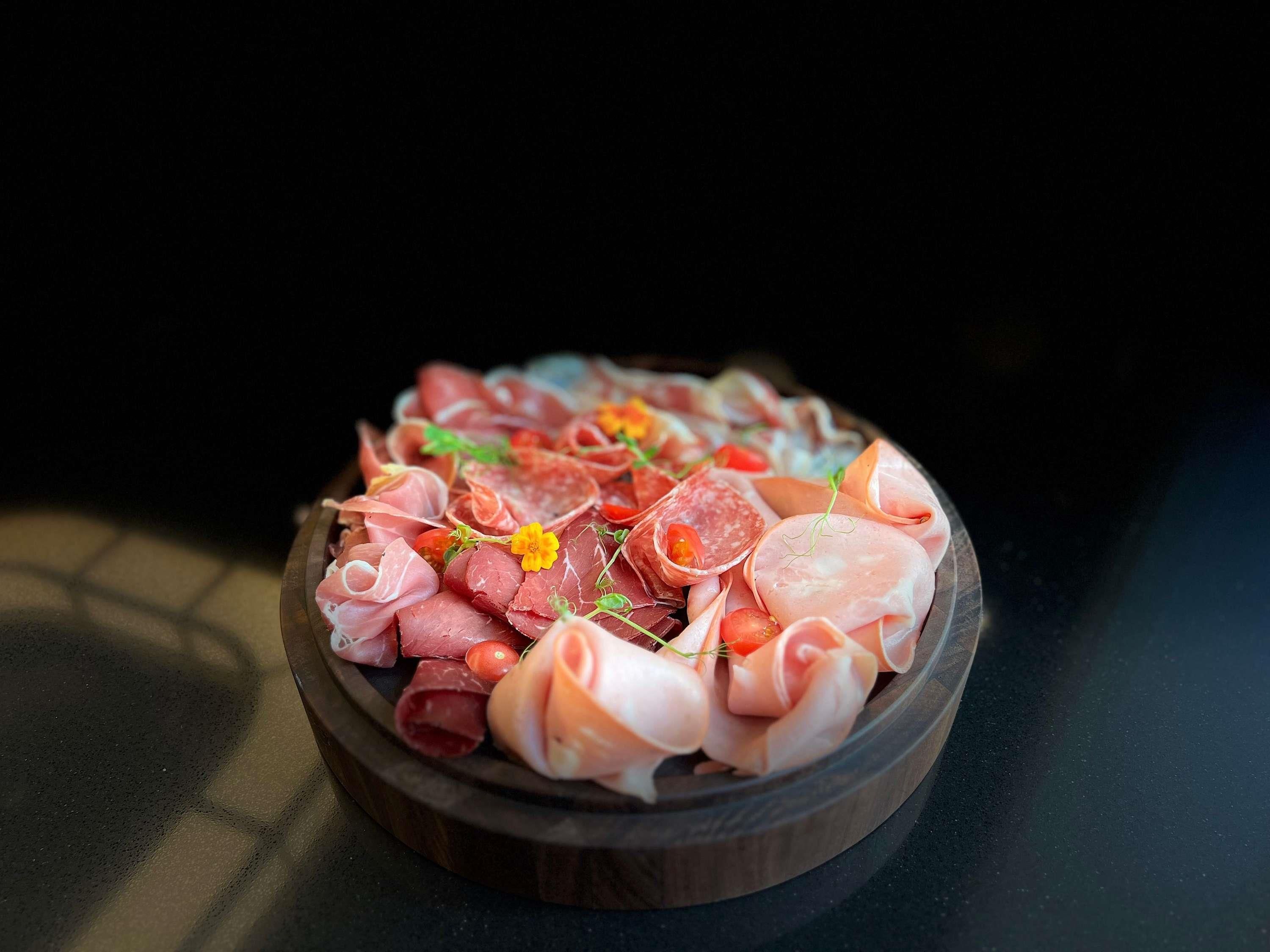 A wooden platter with various types of cured meats and garnishes.