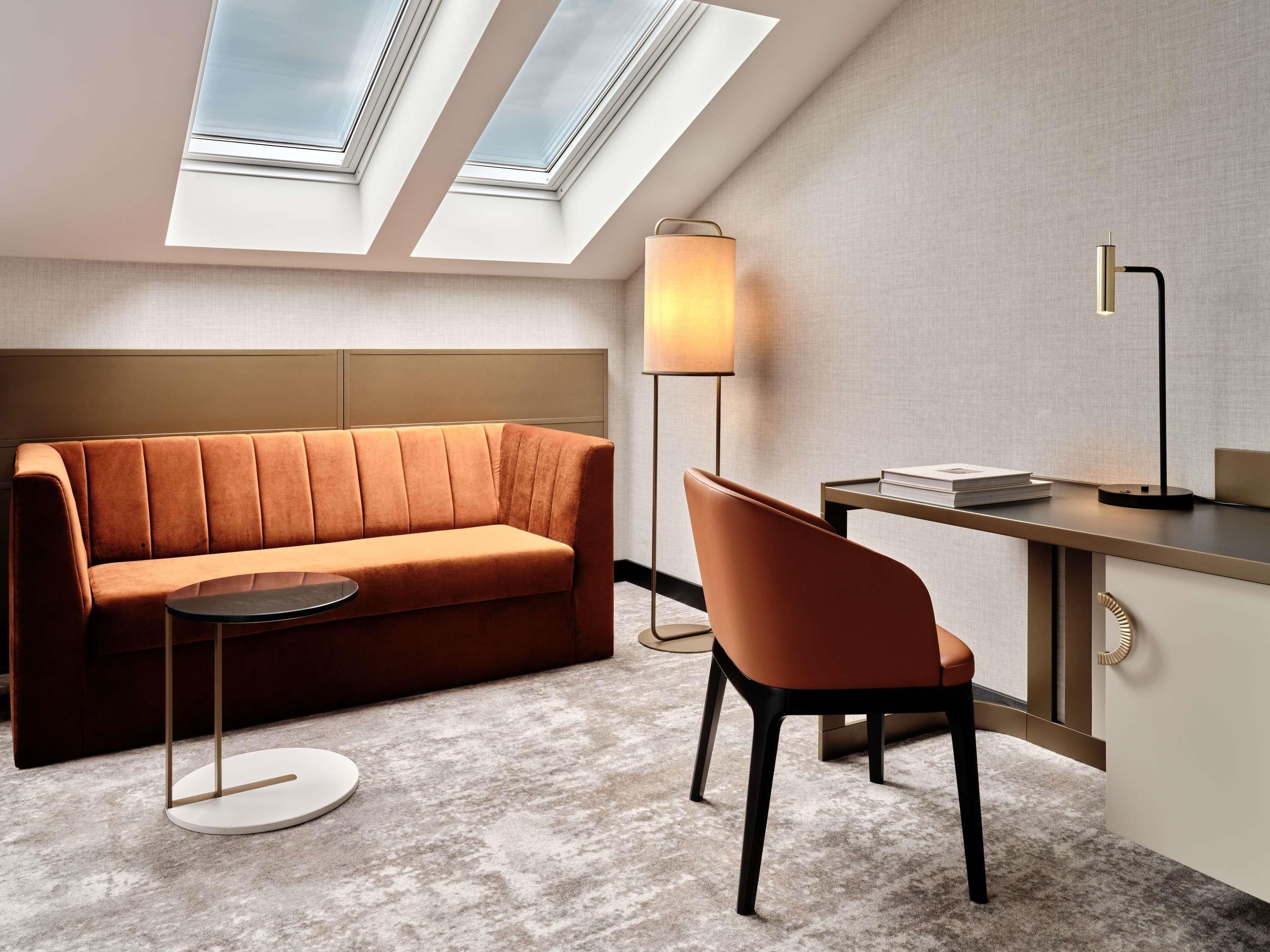 Una habitación moderna con sofá, escritorio, silla, lámpara y tragaluces.