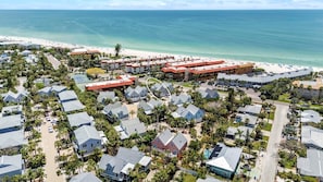 An aerial view of a coastal resort with beachfront properties, a tennis court, and a pool area.