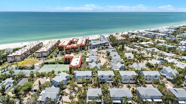 A coastal resort with multiple bungalow-style buildings, a tennis court, and a beach in the background.